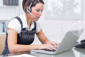 Business woman wearing headset and using laptop in office