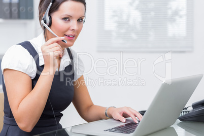 Female executive wearing headset while using laptop at desk