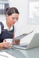 Business woman with coffee cup and laptop reading paper at offic