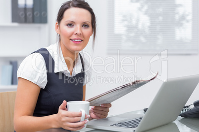 Portrait of executive with coffee and laptop reading paper at of
