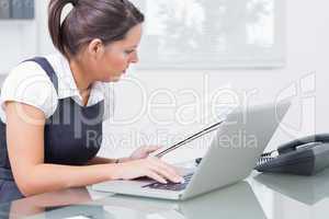 Business woman reading paper while using laptop at office