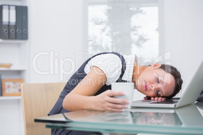 Business woman with coffee cup resting head on laptop at office