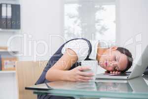 Business woman with coffee cup resting head on laptop at office