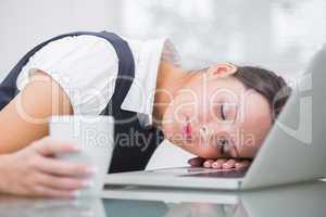 Business woman with coffee cup resting head on laptop at office