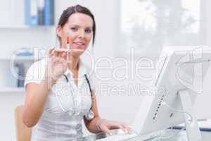 Doctor holding an injection in front of computer at clinic