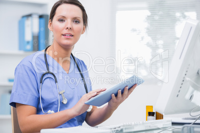 Portrait of surgeon using digital tablet in front of computer at