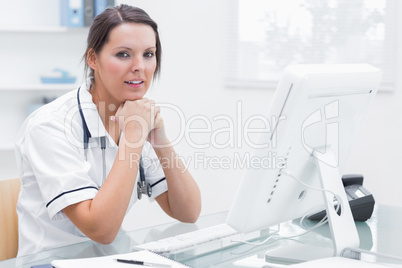 Nurse with hands under chin in front of computer at clinic