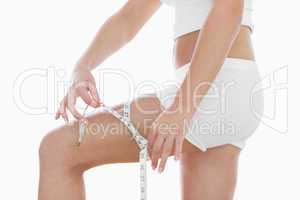 Midsection of woman measuring thigh