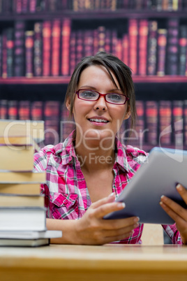 College student with digital tablet and stack of books at librar