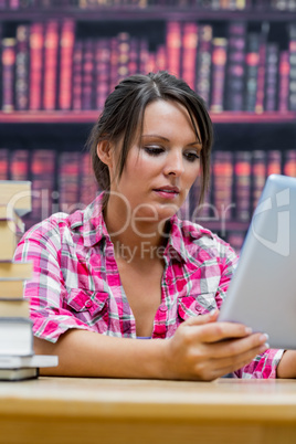 College student using digital tablet with stack of books at libr