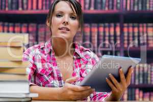 College student with digital tablet and stack of books at librar