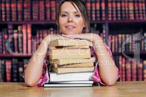 Portrait of college student sitting with stack of books in libra