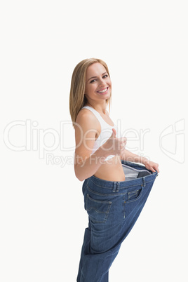 Woman wearing old pants after losing weight and gesturing thumbs