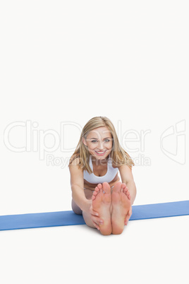 Portrait of happy woman performing stretching exercise on yoga m
