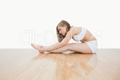 Side view of young  woman stretching on hardwood floor