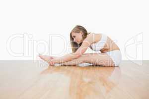 Side view of young  woman stretching on hardwood floor