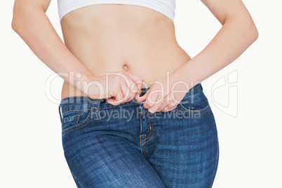 Midsection of slim woman buttoning jeans
