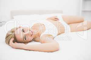 Smiling woman in undergarments lying in bed