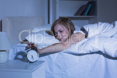 Woman in bed extending hand to alarm clock