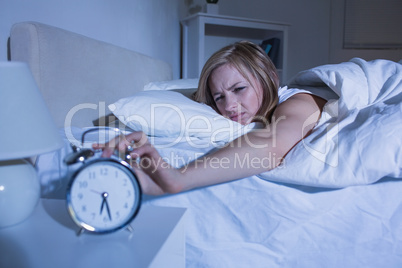 Woman in bed extending hand to alarm clock