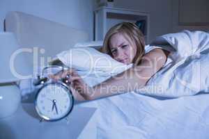 Woman in bed extending hand to alarm clock