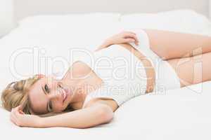Smiling semi dressed woman lying in bed