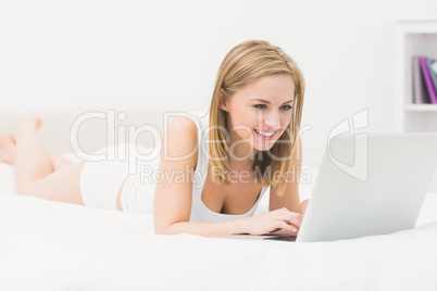 Beautiful happy woman lying in bed and using laptop