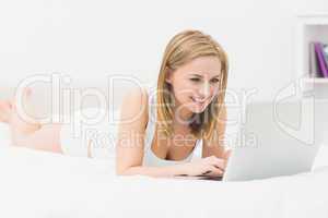Beautiful happy woman lying in bed and using laptop