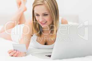 Casual young woman doing online shopping in bed