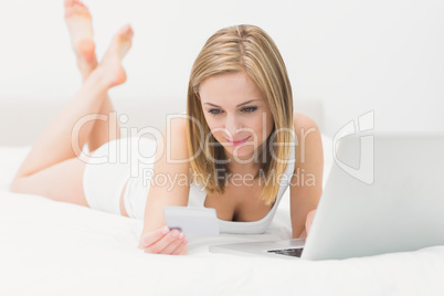 Casual young woman doing online shopping in bed