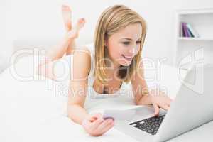 Casual young woman doing online shopping in bed