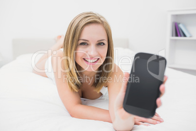 Portrait of casual woman showing new smartphone in bed