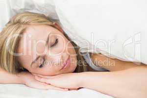 Close-up of beautiful woman under sheet with eyes closed in bed