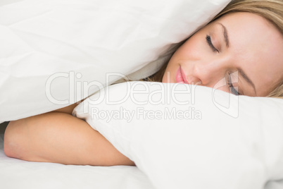 Close-up of beautiful woman under sheet with eyes closed in bed