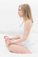 Side view of woman sitting in lotus position in bed