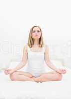 Woman sitting in lotus position on bed