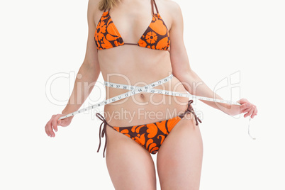 Midsection of young woman in bikini measuring waist