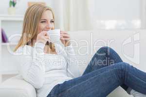 Woman drinking coffee as she looks away on couch