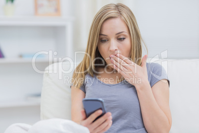 Casual shocked woman looking at cellphone at home