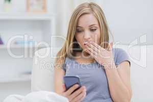Casual shocked woman looking at cellphone at home