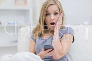 Portrait of casual shocked woman with cellphone at home