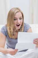 Shocked woman reading letter in living room