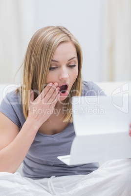 Shocked woman reading letter in living room