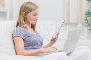 Casual woman using laptop and holding book in living room