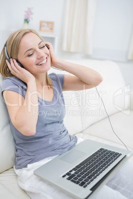 Happy woman listening music through headphones with laptop