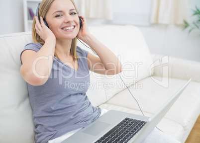 Happy woman listening music through headphones with laptop