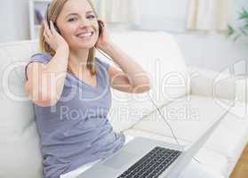 Happy woman listening music through headphones with laptop