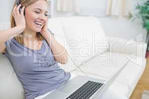 Happy woman listening music through headphones with laptop