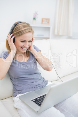 Happy woman listening music through headphones with laptop