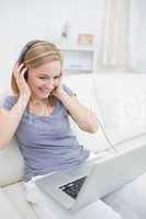 Happy woman listening music through headphones with laptop